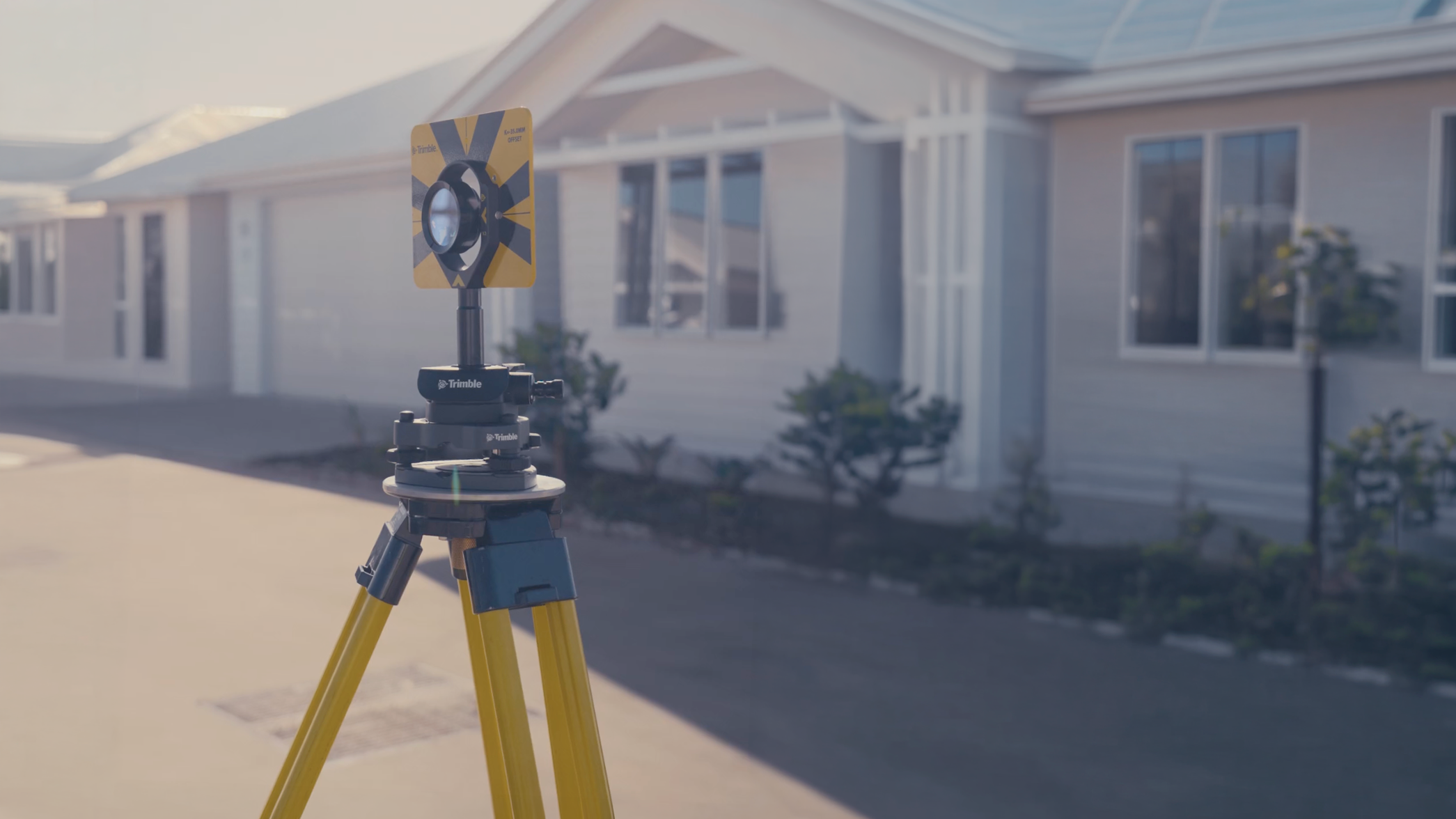 Total Station survey equipment set up on a road, aimed toward residential houses for property boundary measurements.