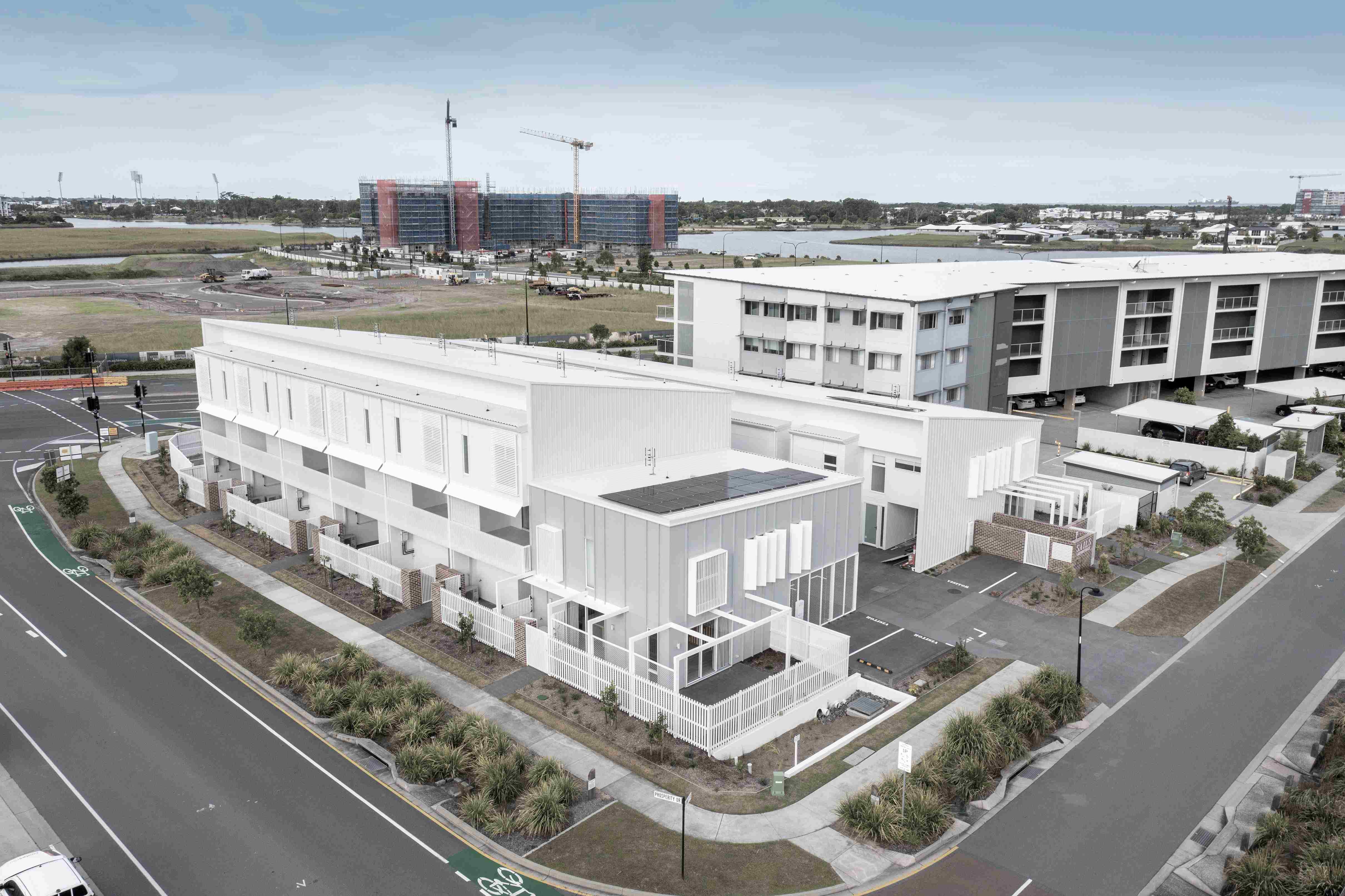 An aerial photo of a multi-story, modern building with a flat roof, surrounded by paved areas and some sparse landscaping.