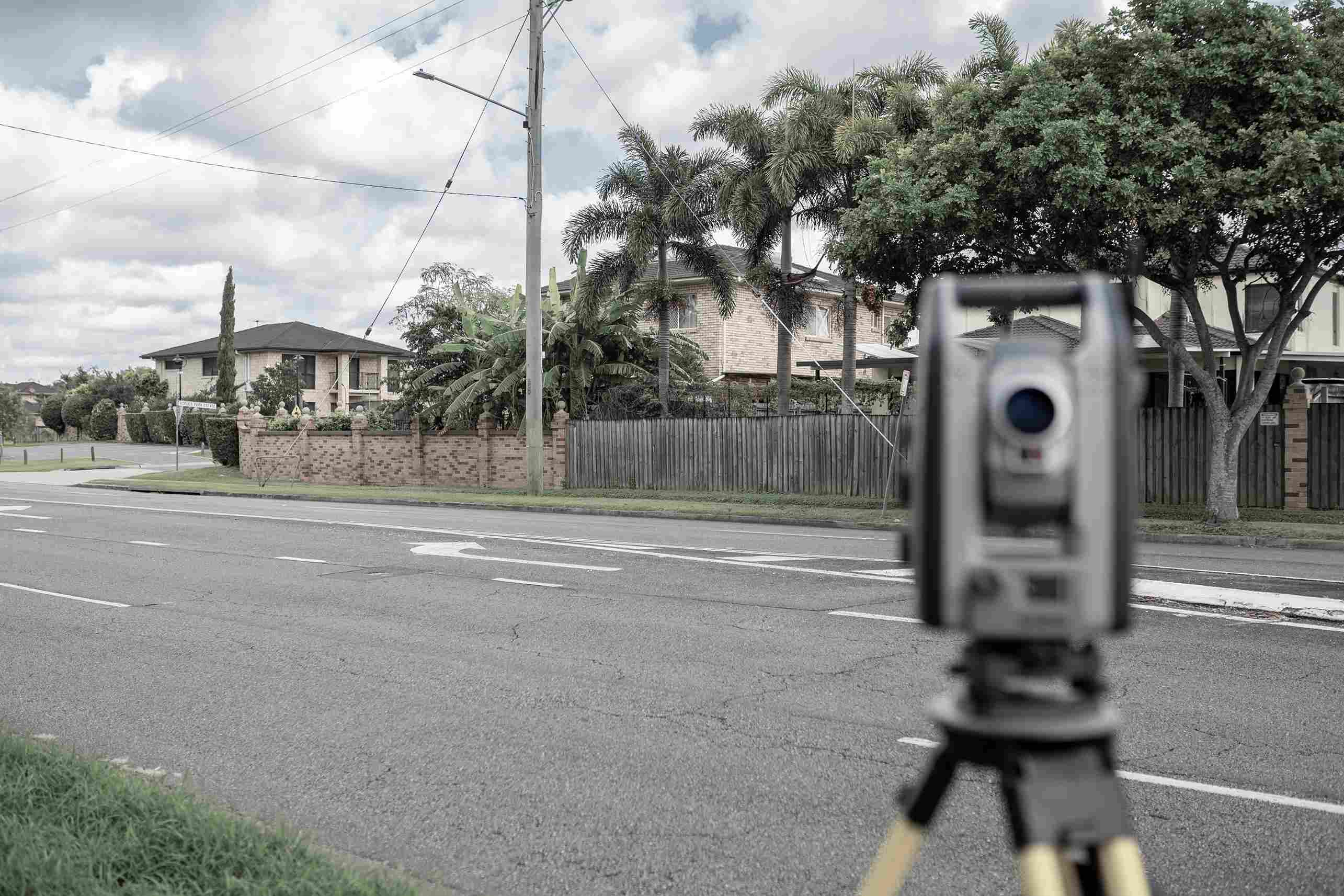 Total Station survey equipment set up on a road, aimed toward residential houses for property boundary measurements.
